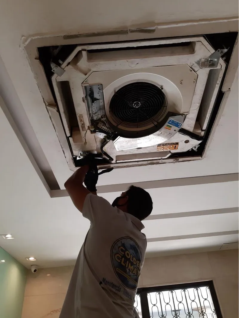 Técnico da Colder Climate com a camiseta da empresa abrindo um ar-condicionado cassete no teto