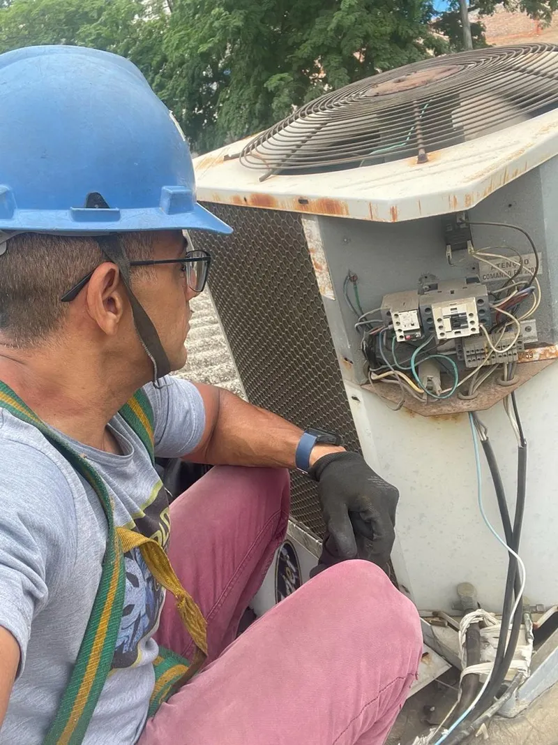 Técnico da Colder Climate, de capacete e luvas, avaliando o quadro elétrico de uma condensadora